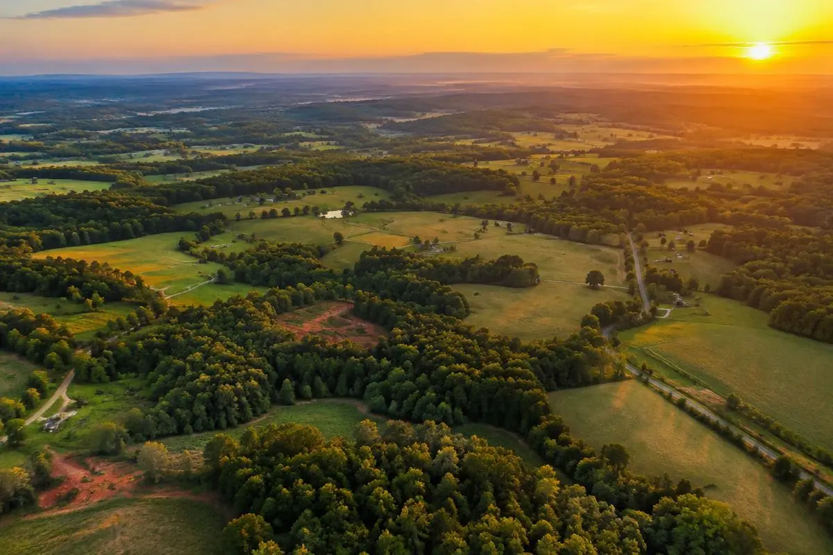 High aerial view at sunset over rolling Piedmont countryside with woodlots, pastures, small red clay clearings and rural roads